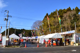 道路沿いの会場に白いテントのお店がたくさん並び、色とりどりの旗が風になびくイベント会場の様子の写真