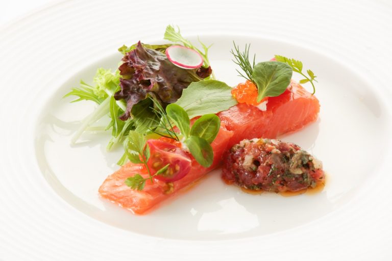 白いお皿の上に、サーモンの刺身や、イクラ、トマト、ラディッシュ、葉物野菜が美しく盛り付けられている、銀鮭のコンフィの写真