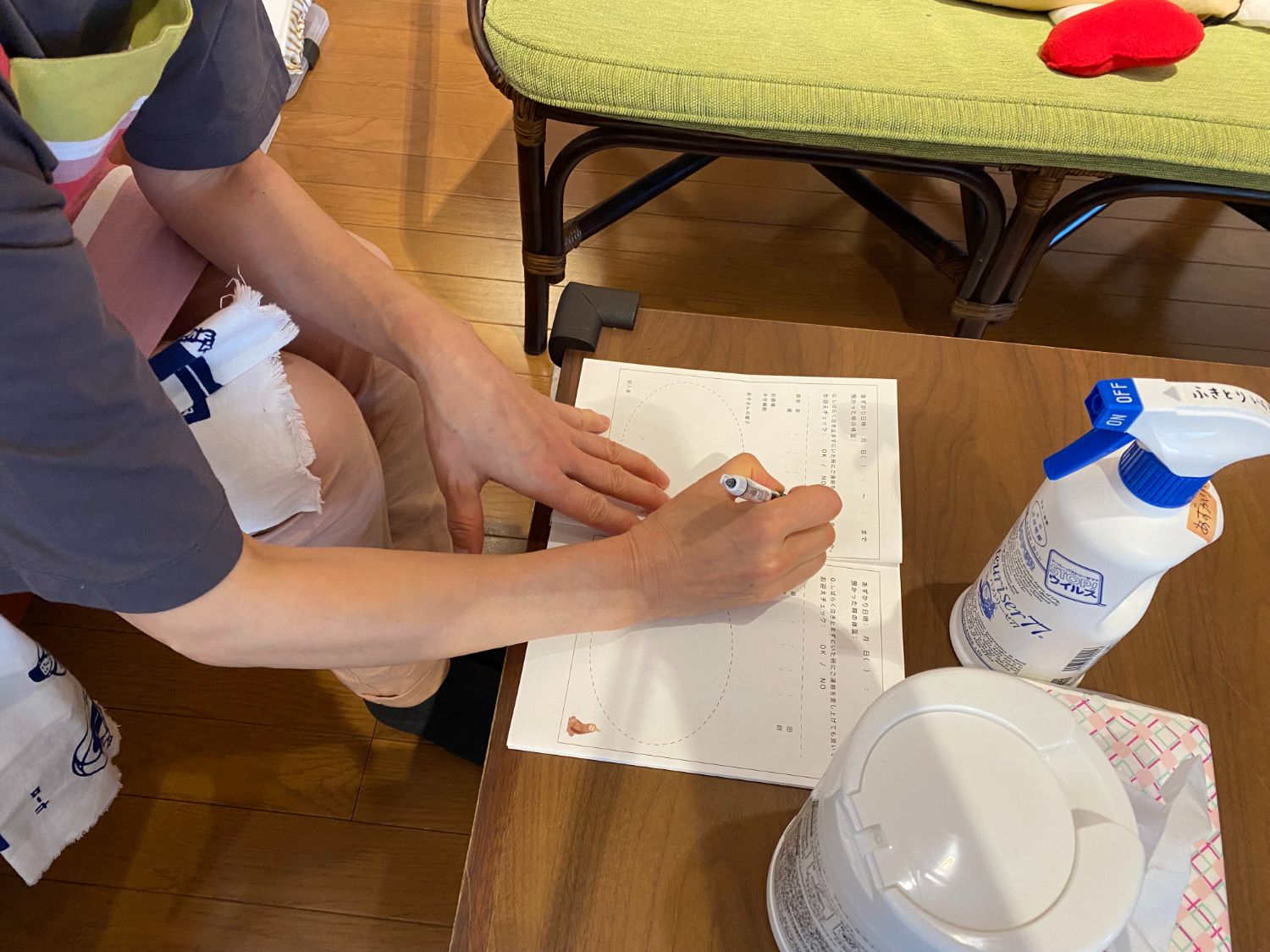 テーブルに座った母親が、「あずかりあいっこ」に関する書類にボールペンで必要事項を記入している手元の様子の写真