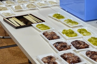 室内のテーブルの上に、ずんだあんやあんこなどで味付けされた餅が白いトレーに入って並べられている正月の振る舞い餅の写真