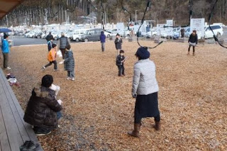 子どもたちが寒空の下で元気に外遊びをしており、保護者たちが見守っている写真