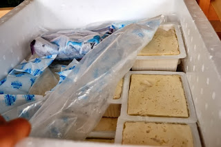 発泡スチロールの保冷箱に保冷剤と一緒に丁寧に並べられた白いパック入りの手作り豆腐入っている写真