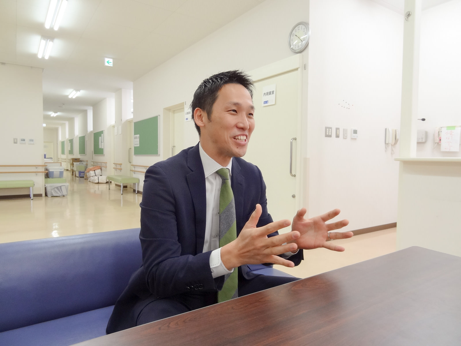 テーブルに向かって青いソファに座った片山さんが手振りを交えてにこやかに話をしている写真