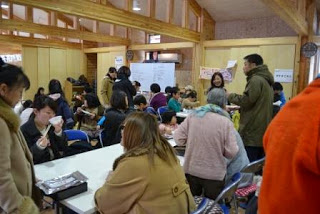 集会所に大勢の住民が集まり、机を囲んで餅を食べながら交流している和やかな様子を写した写真