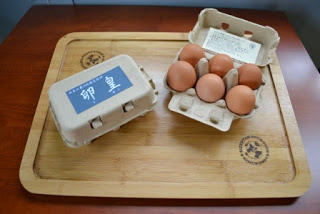 木製トレーの上に新鮮な茶色い卵が6個入ったパックと卵皇と表記された卵パックが置かれている写真