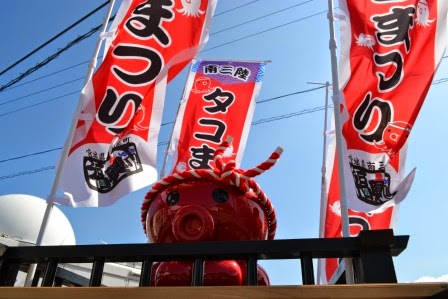 空にたなびいている「南三陸タコまつり」と書かれた赤いのぼりが山車の上の四隅に設置され、赤いタコのオクトパス君が乗っている様子no写真