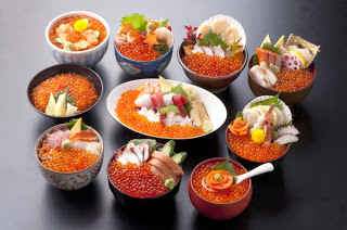 それぞれにいくらや刺身、貝などの新鮮な具材がたっぷり盛られている、色とりどりの海鮮丼が10種類ほど黒いテーブルの上に並んでいる南三陸キラキラ丼の写真