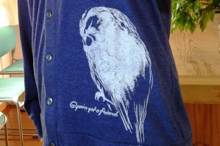 英字と大きく描いた白いフクロウのイラストが描かれている青いカーディガンをアップで撮影した写真