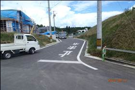 道路に「止まれ」の白文字が大きく書かれた交差点で、左側では建築中の建物や軽トラックが見える工事現場の写真