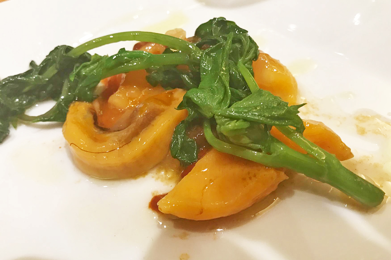 白い器の上に黄色のホヤの身と緑色のシドケが美しく盛り付けられている料理の写真