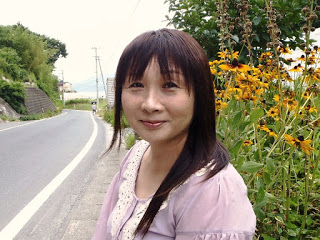 黄色の花の前でピンクの服を着て笑顔の遠藤さんの写真