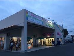 薄暗くなってきた夕方の空の下、大きな看板が掲げられた物産館の入り口に親子連れが出入りしている様子の写真