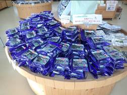 ポップが貼られた円柱型の木製の陳列台の上に、紫色の包装で包まれた沢山の商品が並べられている写真