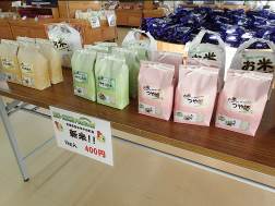店内に設置された長机にポップが貼られ、黄色・緑・ピンクなど色とりどりの袋に入った新米が並べられている写真