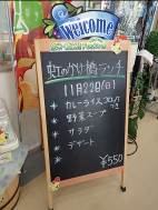 「Welcome」と英語で書かれたカラフルな装飾がある木枠の黒板に、「虹のかけ橋ランチ」と題されたメニューが書かれていて、カレーライスコロッケつき、野菜スープ、サラダ、デザートが含まれ、価格は550円と表示されている写真