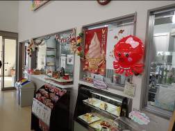 小さな店舗またはカフェの店内で、スイーツが並ぶショーケースや販売カウンターがあり、大きな赤いタコのバルーンやソフトクリームのポスター、カウンター上部にはガーランドなどの装飾が施されている様子の写真