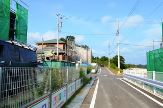 住宅建設中の建物が左側に並び、細い舗装道路がまっすぐ奥へ続いている造成地の写真
