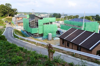 緑に囲まれた坂道の周囲に建設中の家々が建っている造成地を、高台から撮影した写真