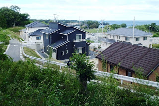 完成した複数の戸建て住宅が並び、その奥に海がうっすらと見える住宅地を高台から撮影した写真