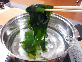 きれいな緑色に変化した生わかめを熱湯の鍋からだしている写真
