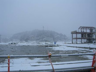 手前に骨組みだけの建物が写り、吹雪によって視界が白くかすんで遠くが見えない様子を写した写真