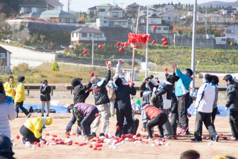 参加者がカゴに向かって赤いボールを投げ入れている玉入れ競技の様子の写真