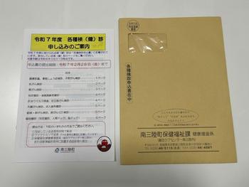 「令和7年度各種検診(健診)申し込みのご案内」の用紙とA4サイズの茶封筒が並べて置かれている写真