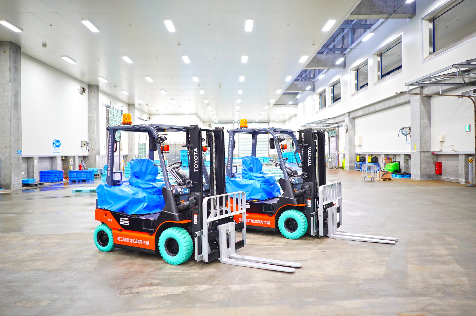 明るい倉庫の室内に同じ型の電動フォークリフトが2台並んでいる様子を写した写真