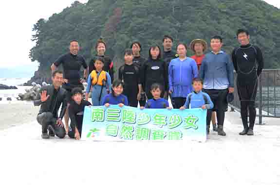 「南三陸少年少女自然調査隊」と書かれた横断幕を持ちウエットスーツを着た子供たちが並んでいる集合写真