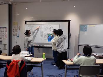 ホワイトボードに書かれた文字を指差した女の子が発表している子どもたちの写真