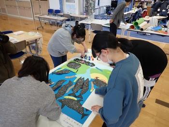 大きなポスターに魚の絵や文字を書き込んでいる写真