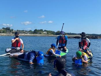 海の上でボードに乗りながら海中をのぞいている子どもたちの写真