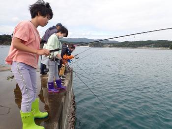 防波堤に並んで釣りを楽しむ子どもたちの写真