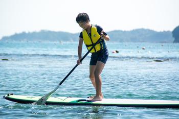 海の上をパドルボードに立ってこいでいる男の子の写真