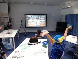 室内でスクリーンを見ながら拍手をしたり両手を上げている子どもたちの写真