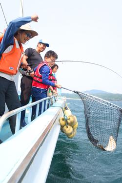 船の上で大きな網を使って魚をすくい上げている子どもたちの写真