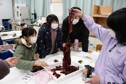 子どもたちが教室で大きな赤い海藻を観察している写真