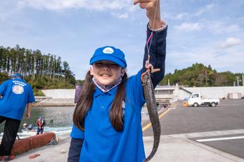 釣り上げた魚を笑顔で持ち上げて見せる女の子の写真