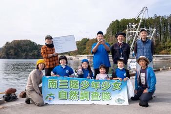 港で「南三陸少年少女自然調査隊」の横断幕を掲げて記念撮影する子供たちの写真
