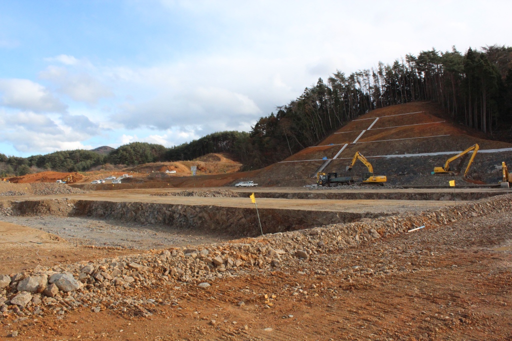 山の斜面が切り取られ土肌が見えており、数基のクレーン車が作業を行っている様子の写真