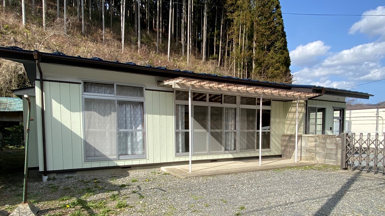 林を背にした静かな場所に建つ、白っぽい外壁と大きな窓が特徴の一戸建て鏡石定住促進住宅の外観写真