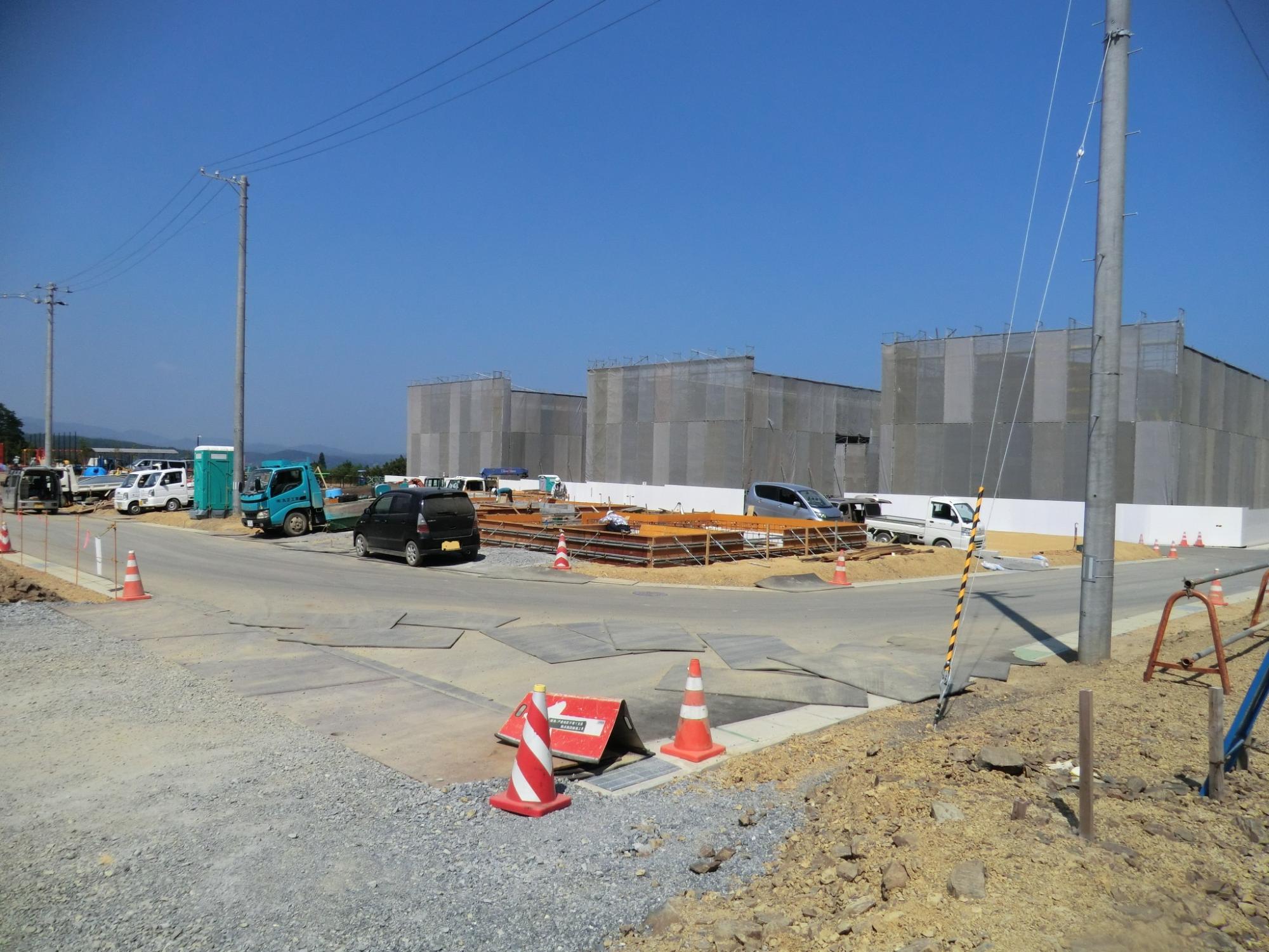 複数の建設中の建物がネットで覆われ、手前には工事用車両が並び、道路の舗装や整地作業が進められている様子が見える、災害公営戸倉住宅を作っている写真