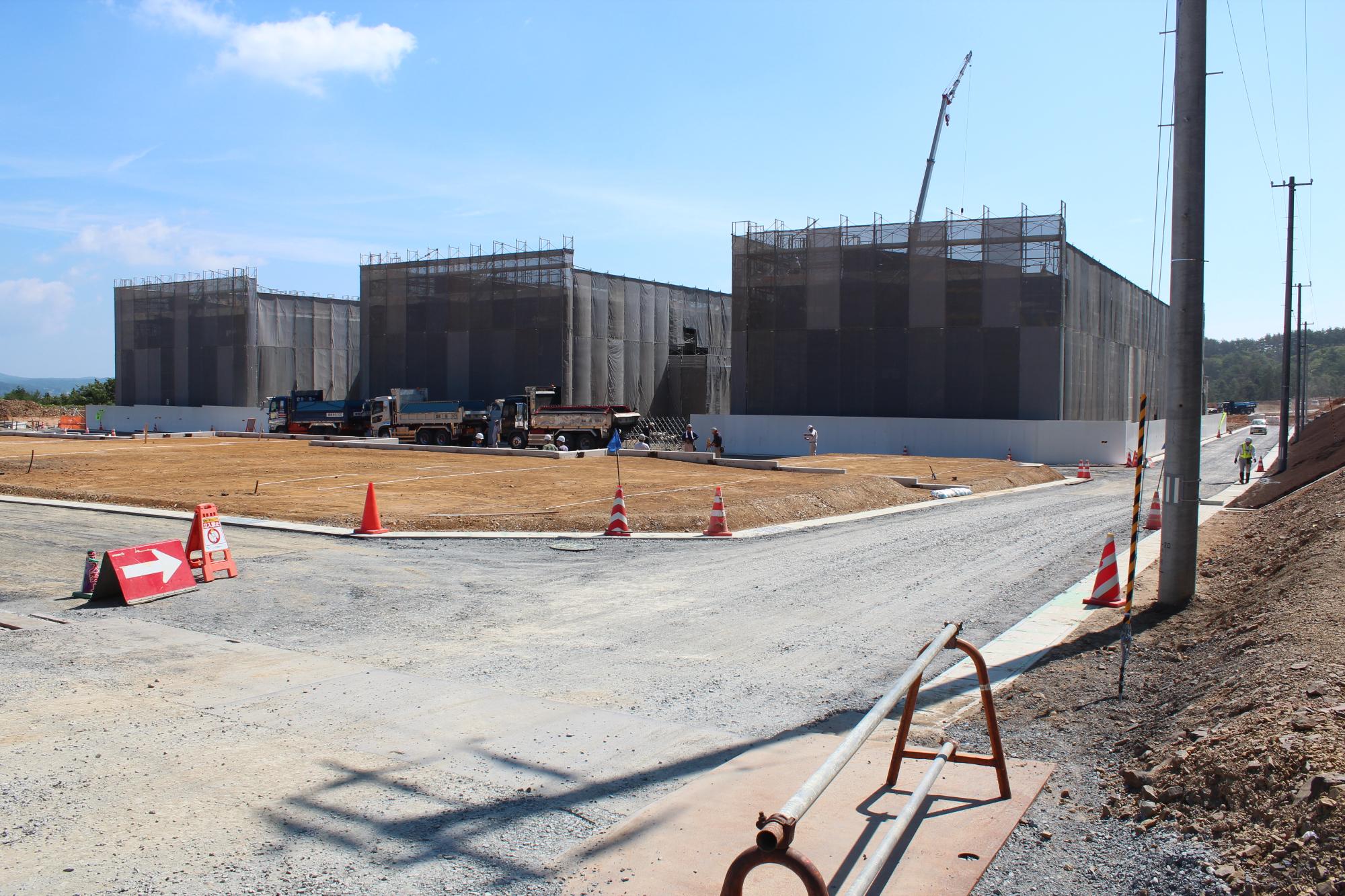 三つの建物が足場とネットに覆われて整然と並び、道路や歩道の整備も進んでいる様子が手前に広がる、完成に近づいた災害公営戸倉住宅を作っている写真