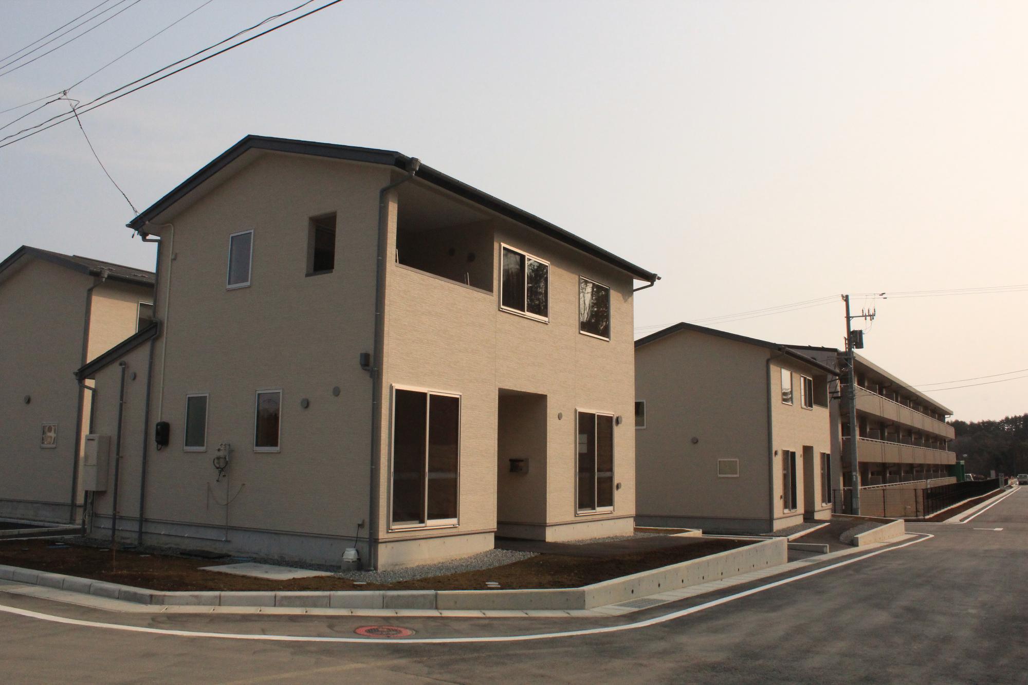 ベージュ系の外壁と大きな窓が特徴の、2階建ての一戸建て住宅の前にきれいに舗装された道路が通っている新しく整備された住宅地の様子の写真