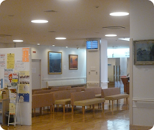 淡い黄色の長椅子がたくさん設置され、壁には絵画が飾られている待合室の写真