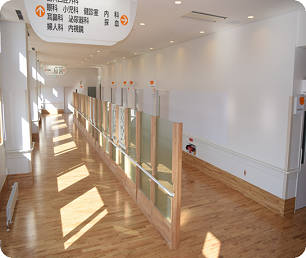 自然光の入る明るい廊下の上部に施設の案内看板があり、廊下の中央には通路の仕切りが設置されている様子の写真