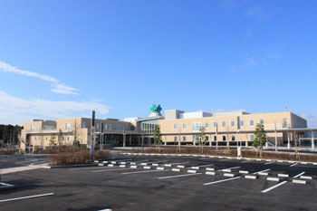 広い駐車場と植木が整備された奥には、ベージュ色の大きな病院が建っている様子の写真