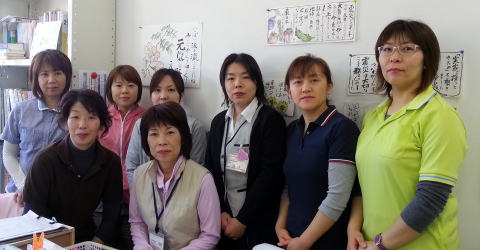 室内でポロシャツなどを着た8人の女性が並んだ集合写真