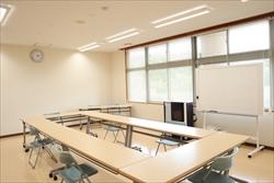 ロ型に机といすが設置され、窓際にホワイトボードが置かれた明るい会議室内の写真