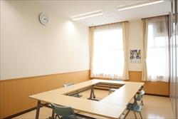 ロ型に設置された机といすがありカーテンのあるこじんまりとした研修室内の写真